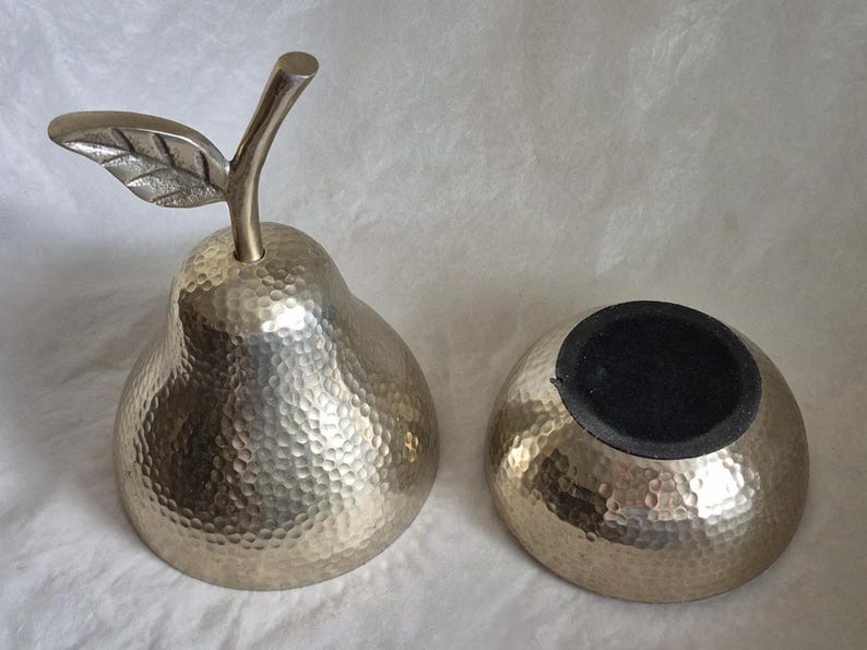 May include: A decorative pear-shaped container and a separate bowl, both with a hammered metal finish. The pear has a stem and leaf detail. The bowl has a black interior. The set is likely for home decor.