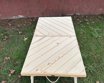 May include: A white wooden folding table with a diagonal wood grain pattern. The table has two white legs and a rope handle.