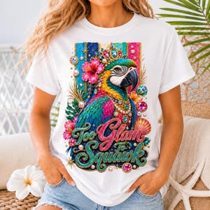 May include: White t-shirt featuring a colorful parrot design with a crown, jewels, and flowers. The text "Too Glam to Squawk" is written in a decorative font. The parrot has blue, green, yellow, and pink feathers.