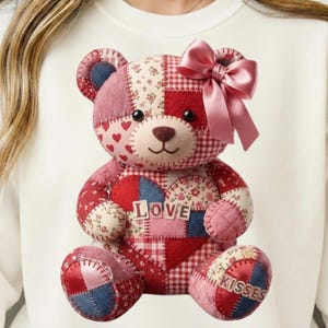 Peut inclure: Un ours en peluche patchwork avec un nœud rose. L'ours est fait de divers tissus rouges, roses et bleus, avec des motifs de cœurs et de fleurs. Le mot "LOVE" est sur la poitrine de l'ours, et "KISSES" sur un pied.