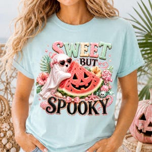 Peut inclure: T-shirt bleu clair avec l'inscription "SWEET BUT SPOOKY". Le motif présente un fantôme portant des lunettes de soleil en forme de cœur, une tranche de pastèque sculptée en forme de citrouille et des éléments floraux.