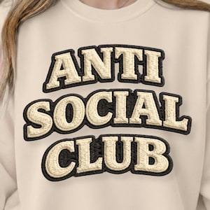 Peut inclure: Sweat-shirt crème avec l'inscription brodée "ANTI SOCIAL CLUB". Les lettres beiges claires sont bordées de noir, créant un contraste saisissant sur le fond neutre. Un vêtement décontracté et confortable.