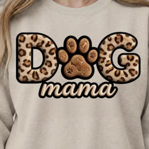 May include: A beige sweatshirt featuring the text "DOG mama" in a playful design. The letters "D" and "G" have a leopard print pattern, with a paw print and bone graphic in the center.