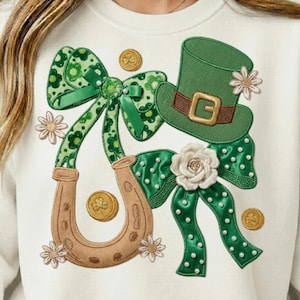 Peut inclure: Sweat-shirt crème avec un motif de la Saint-Patrick. Le motif comprend un chapeau haut de forme vert avec une bande marron, un fer à cheval, des nœuds, des pièces d'or et des accents floraux. Les nœuds ont un motif floral et sont ornés de perles.
