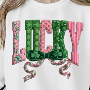 May include: A white sweatshirt with the word "LUCKY" in large, colorful letters. The letters are pink and green, with shamrock accents and a green bow. The design is festive and celebratory.