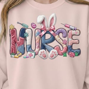 Peut inclure: Sweat-shirt rose avec le mot "NURSE" dans un design patchwork coloré. Les lettres sont décorées d'éléments sur le thème de Pâques, notamment des oreilles de lapin, des empreintes de pattes, des œufs et des fournitures médicales.