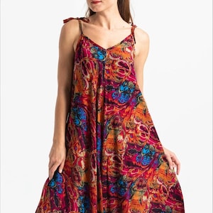 May include: A colorful, flowing jumpsuit with a V-neck and tie straps. The fabric features a vibrant, abstract pattern in shades of red, orange, blue, and yellow. The jumpsuit has a loose, comfortable fit, suitable for warm weather.