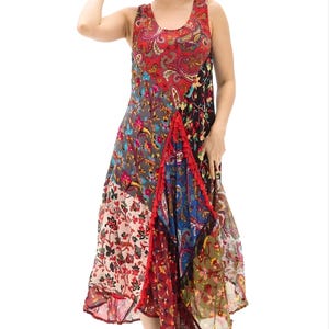 May include: A sleeveless, patchwork maxi dress with a vibrant mix of floral, paisley, and geometric patterns in red, blue, and brown hues. The dress features a flowing skirt and is paired with a matching red sun hat. The model is wearing silver sandals.