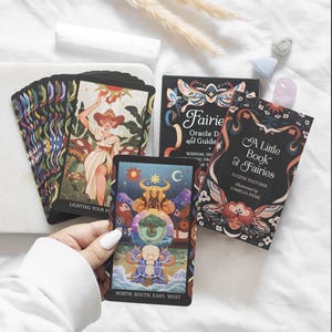 May include: A deck of oracle cards titled Fairies Oracle Deck and Guidebook, featuring a black box with colourful fairy illustrations and the text A Little Book of Fairies by Eugene Fletcher. One card shows a figure with a crystal ball and the text North, South, East, West.