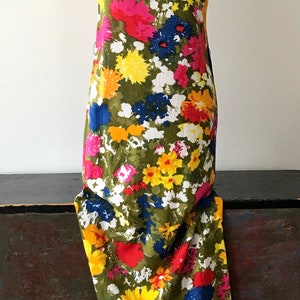 May include: A sleeveless maxi dress with a vibrant floral print. The dress features a variety of colors, including yellow, red, pink, blue, and green. The flowers are large and bold, and the dress has a simple, elegant silhouette.