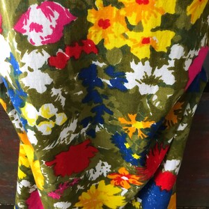 May include: A green fabric with a floral print featuring yellow, red, pink, white, and blue flowers. The fabric has a textured, linen-like appearance.