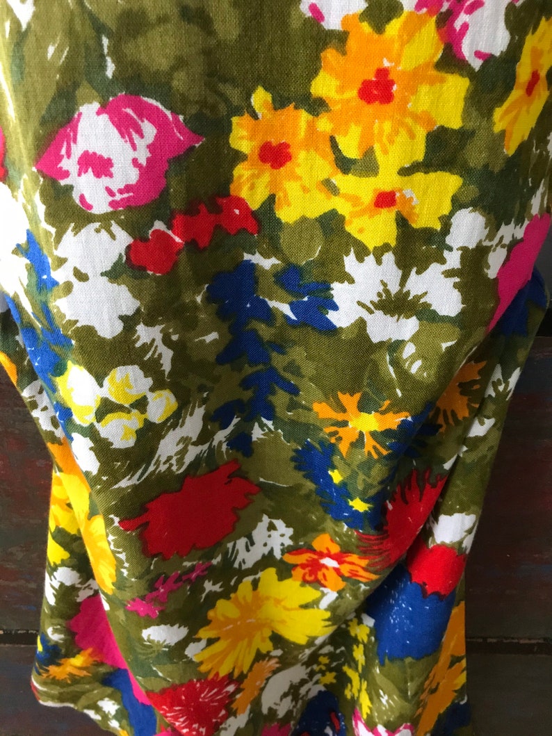 May include: A green fabric with a floral print featuring yellow, red, pink, white, and blue flowers. The fabric has a textured, linen-like appearance.