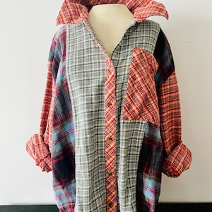 May include: A patchwork flannel shirt with a variety of plaid patterns in red, blue, green, and orange. The shirt has a collared neckline, long sleeves, and button-down front. The sleeves are rolled up.