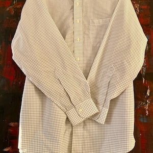 May include: A long-sleeved button-down shirt with a white and navy blue grid pattern. The shirt has a button-down collar, a chest pocket, and buttoned cuffs. The shirt is made of a lightweight fabric.