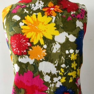 May include: A sleeveless dress with a colorful floral print. The dress features a variety of flowers in shades of red, yellow, blue, pink, and green on a white background.