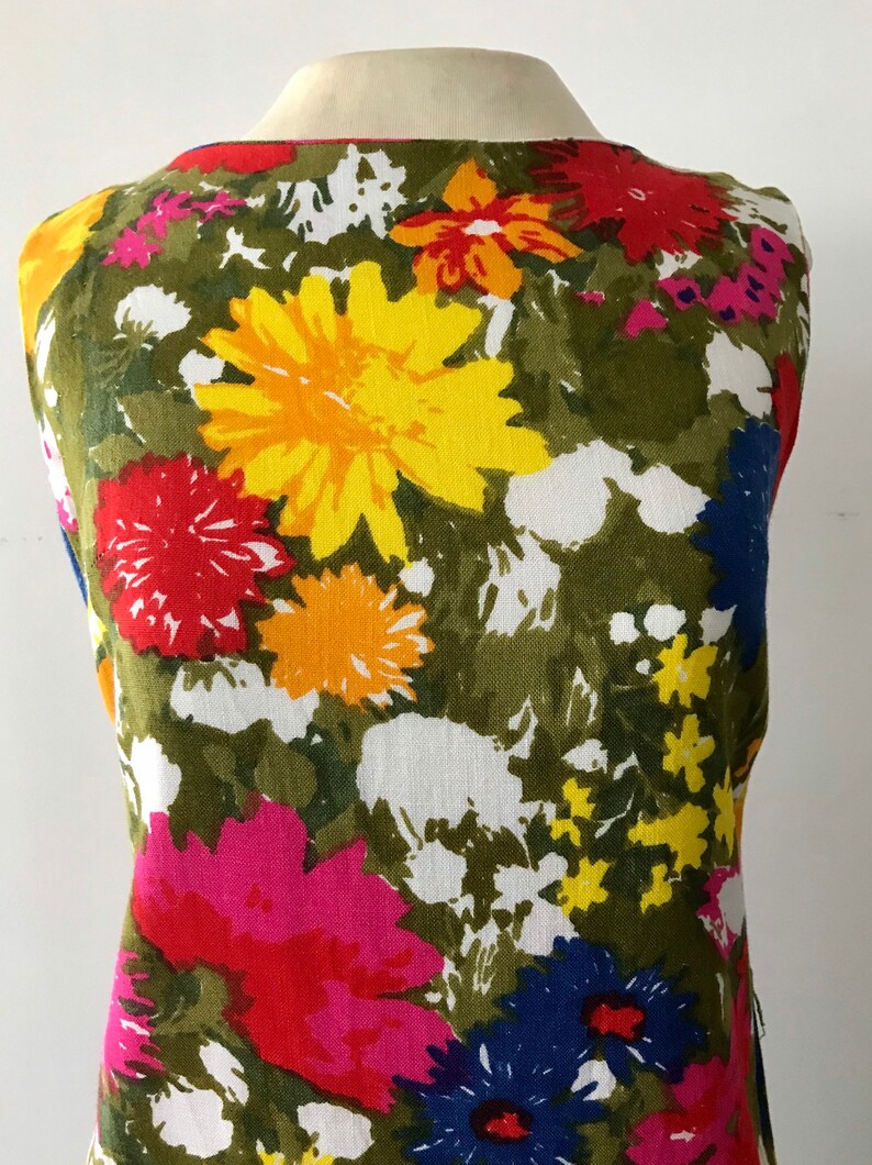 May include: A sleeveless dress with a colorful floral print. The dress features a variety of flowers in shades of red, yellow, blue, pink, and green on a white background.