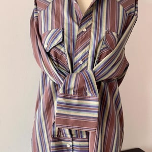May include: A vintage button-down shirt with vertical stripes in shades of brown, blue, and green. The shirt features two chest pockets and buttoned cuffs. The shirt is displayed on a mannequin.