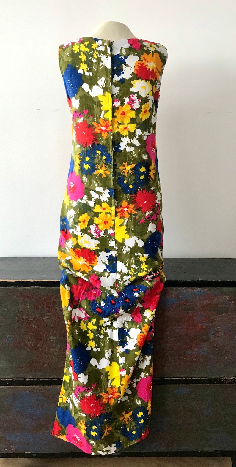 May include: A sleeveless maxi dress with a floral print in shades of pink, red, yellow, blue, and white on a green background.