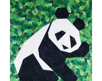 May include: A black and white origami panda bear on a green leafy background. The panda is made of fabric and has a black nose and eyes.