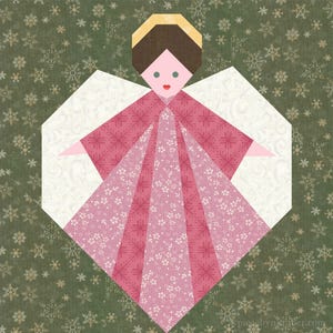 Puede incluir: Un ángel de papel rosa y blanco con halo, alas y cuerpo en forma de corazón. El ángel está sobre un fondo verde con un patrón de copo de nieve.