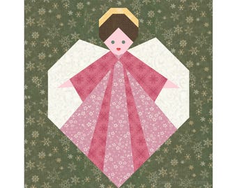 May include: A pink and white paper angel with a halo, wings, and a heart-shaped body. The angel is on a green background with a snowflake pattern.