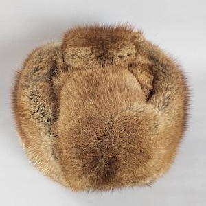 Puede incluir: Un sombrero redondo de piel marrón con una superficie texturizada. El sombrero parece estar hecho de múltiples piezas de piel cosidas. Un cálido accesorio de invierno.