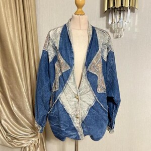 Op de afbeelding: Een vintage spijkerjasje met een uniek patchwork design. De jas heeft een blauwe denim basis met crèmekleurige ruitvormige panelen en paisley accenten. Het heeft een knoopsluiting en wordt op een mannequin gepresenteerd.