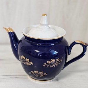 May include: A cobalt blue teapot with a white lid and gold floral accents. The teapot has a rounded body and a spout on one side and a handle on the other.