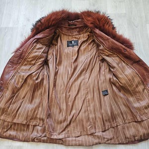 May include: Open brown leather jacket with a fur collar. The interior features a brown striped lining. The jacket has a label that reads "PLACETTE".