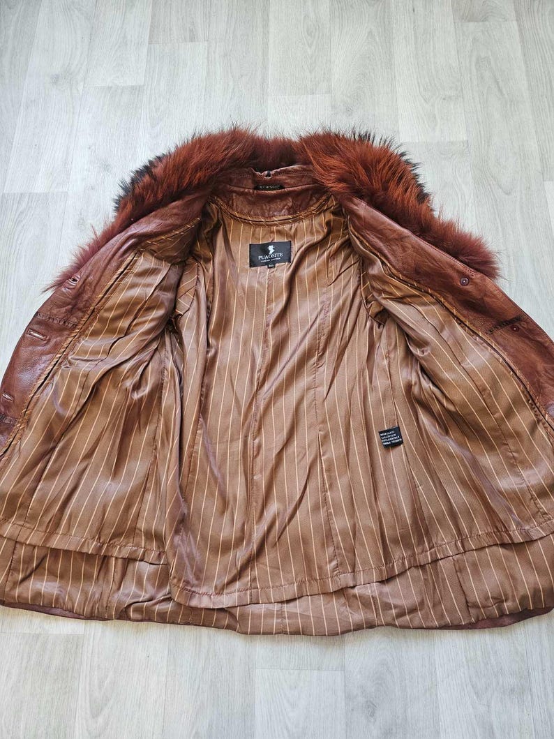 May include: Open brown leather jacket with a fur collar. The interior features a brown striped lining. The jacket has a label that reads "PLACETTE".