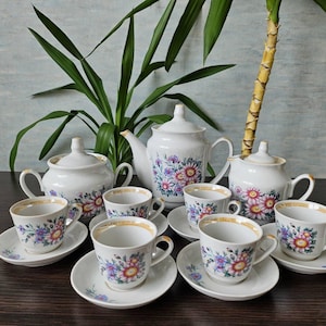 May include: A white porcelain tea set with floral designs. The set includes a teapot, sugar bowl, creamer, and six teacups and saucers.