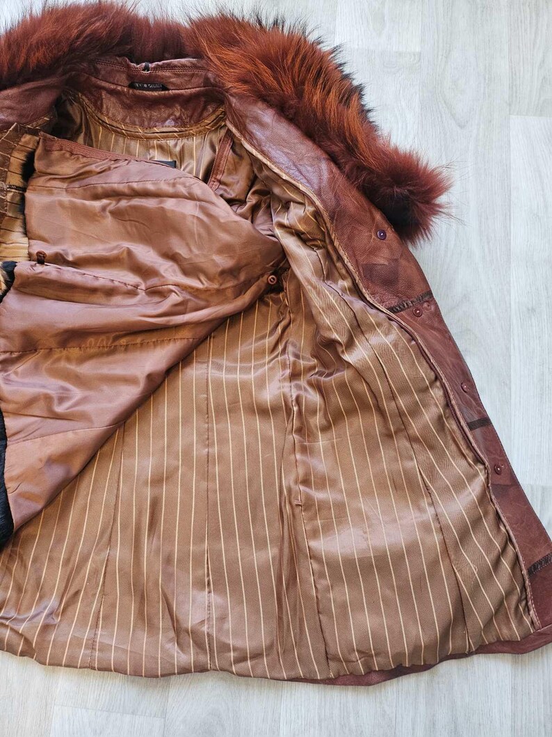 May include: A brown leather coat with a fur collar. The coat is open, revealing a brown striped lining. The fur collar is a reddish-brown color. The coat has button closures and a tailored fit.