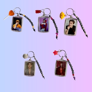 May include: Five clear acrylic keychains featuring photos of a person. Each keychain has a silver ring, a beaded strand with the name "JACKSON", and a charm. Charms include a lollipop, a gummy bear, a lemon, a pom-pom, and a star.