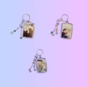 May include: Three clear acrylic keychains with silver key rings. Each keychain features a romantic illustration of two people. Each keychain has a beaded charm with pastel-colored beads and a heart charm.