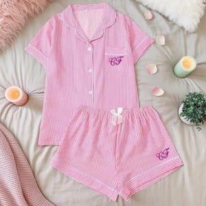 Puede incluir: Conjunto de pijama rosa a rayas. La parte superior de manga corta tiene una botonadura frontal y un bolsillo en el pecho con iniciales bordadas. Los pantalones cortos a juego tienen un lazo y iniciales bordadas. El conjunto está hecho de una tela suave y ligera.