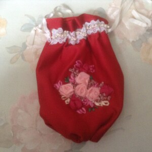 May include: Red fabric pouch with a white lace trim and pink embroidered flowers.
