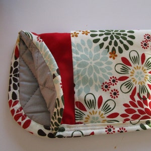 May include: A quilted pot holder with a red, white, and green floral print. The pot holder is made of fabric and has a quilted lining.