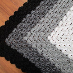 Pu&ograve; includere: Una coperta all'uncinetto con un gradiente di nero, grigio e bianco. La coperta &egrave; realizzata con un delicato motivo a punto e ha un bordo a scalare.