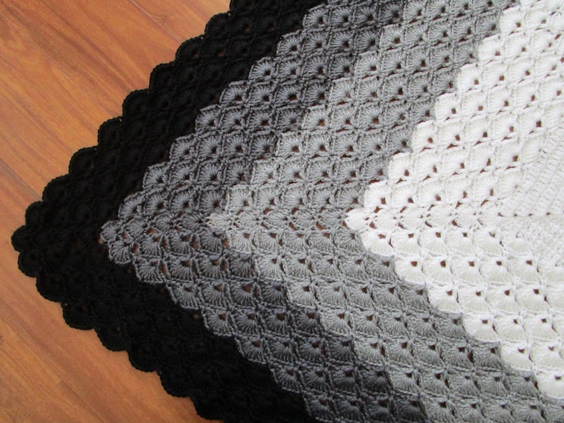 Pu&ograve; includere: Una coperta all'uncinetto con un gradiente di nero, grigio e bianco. La coperta &egrave; realizzata con un delicato motivo a punto e ha un bordo a scalare.