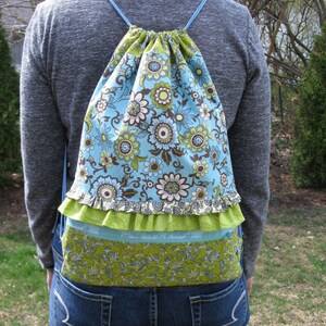 May include: A blue and green floral drawstring backpack with a ruffled trim. The backpack is made of fabric and has a cinched top.