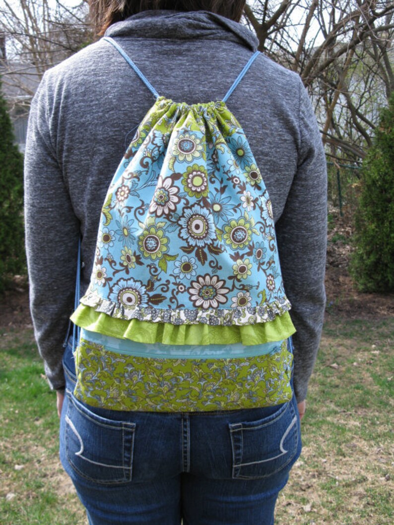 May include: A blue and green floral drawstring backpack with a ruffled trim. The backpack is made of fabric and has a cinched top.