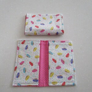 May include: A pink and white fabric wallet with a donut and sprinkles pattern. The wallet is folded in half and has a pink fabric lining.