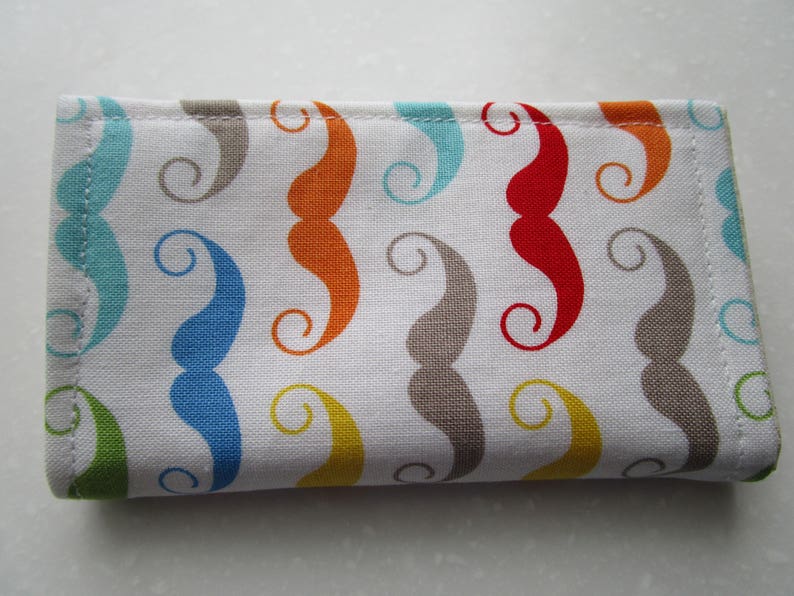 May include: A white fabric wallet with a colorful mustache pattern. The mustaches are in shades of blue, green, orange, red, and gray.