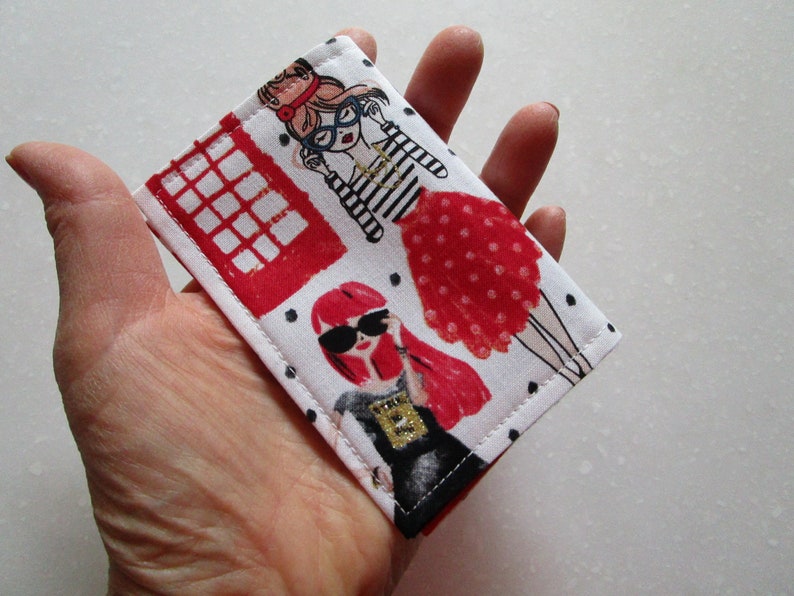 Puede incluir: Un porta tarjetas de tela blanca con una cabina telef&oacute;nica roja, lunares negros y dos mujeres de dibujos animados con vestidos rojos y gafas de sol.