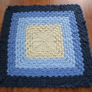 Pu&ograve; includere: Una copertina per neonati all'uncinetto con un design quadrato in tonalit&agrave; di blu e beige.