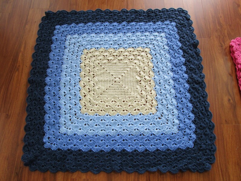 Pu&ograve; includere: Una copertina per neonati all'uncinetto con un design quadrato in tonalit&agrave; di blu e beige.