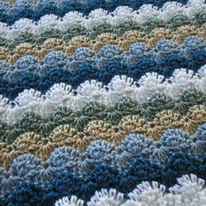 May include: A crocheted blanket with a wave design. The blanket displays rows of different colours, such as white, blues, greens, and tan. The texture is evident, with each stitch forming a scalloped edge. The overall appearance is a cosy, textured textile.