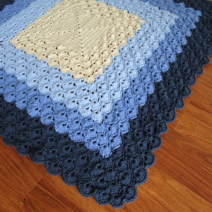 Pu&ograve; includere: Una copertina per neonati all'uncinetto con un motivo a rombi in tonalit&agrave; di blu e beige.