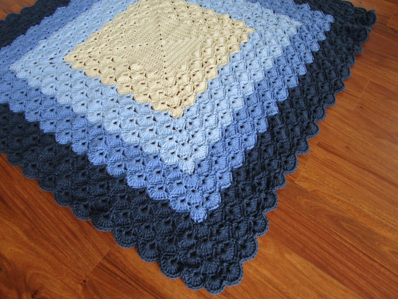 Pu&ograve; includere: Una copertina per neonati all'uncinetto con un motivo a rombi in tonalit&agrave; di blu e beige.