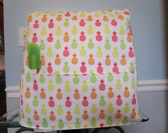 May include: White kitchen appliance cover with a pineapple pattern in shades of green, yellow, orange, and pink. The cover has a pocket on the side for a spatula.